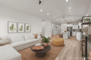 A modern living room with a white sectional sofa, round coffee table, orange ottoman, and wall art of green leaves sets the tone for new beginnings, seamlessly connected to a bright kitchen with white cabinets and stainless steel appliances. “Virtually Staged” in corner.