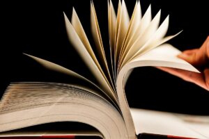 A close-up of a hand flipping through the pages of an open book, with the pages fanned out against a black background—an inviting scene perfect for cozy season.