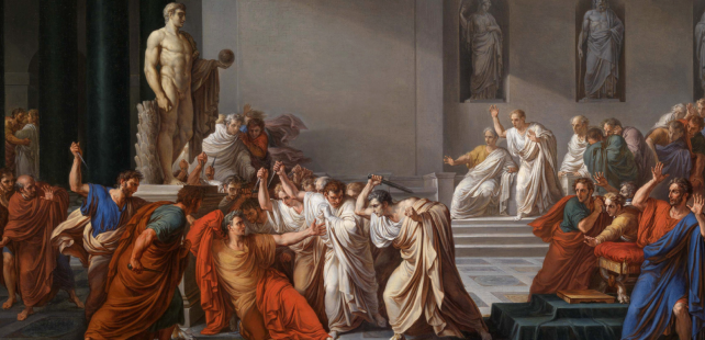 A group of men in ancient Roman robes surround and attack a central figure with daggers inside a grand hall during the Ides of March, while others watch in shock; large statues and columns loom in the background.