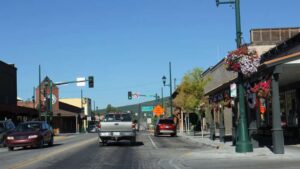 A small town main street with cars, traffic lights, potted flowers, and various shops—including a visible Starbucks—basks in the steady momentum of daily life under clear February light and a bright blue sky.