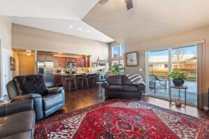 Bright living room with dark leather furniture, a large red patterned rug, wood floors, and an open kitchen. Sliding glass doors lead to a patio—perfect for new beginnings and intentional gatherings—with a view of a fenced yard.