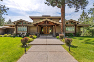 A large Craftsman-style house with wood siding, a covered front porch, and exposed beams sits amid a green lawn—an inviting sight for anyone starting their home buying journey. A wide walkway leads to the main entrance under a partly cloudy sky.
