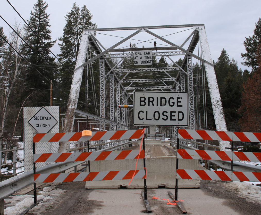 A metal bridge blocked by orange and white barricades and a “BRIDGE CLOSED” sign, with a “SIDEWALK CLOSED” sign on the left. Snow dusts the scene, and bare trees hint at Fall’s arrival in this October Update.