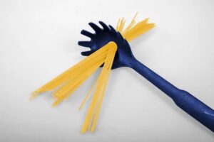 A blue spaghetti server holding uncooked spaghetti noodles, with some strands resting in the slots of the utensil, set against a plain white background—capturing a sense of new beginnings and intention in every detail.