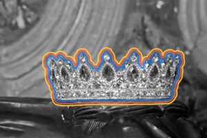 A sparkling diamond crown with blue and orange outlines rests on a black-and-white background featuring a statue’s hand and intricate carvings, capturing the elegance of July Journeys.