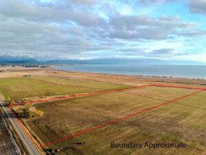 Aerial view of a large, rectangular plot of farmland outlined in red near a road, with open fields and distant mountains. Under the partly cloudy sky, signs of Spring hint at new opportunities. Text reads Boundary Approximate.