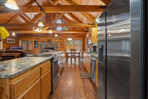 Spacious log cabin kitchen with wooden cabinets, stainless steel appliances, stone countertops, and high vaulted ceiling. Enjoy a warm, rustic atmosphere—perfect for entertaining or relaxing after exploring the Flathead Valley Spring Market.