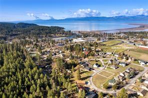 Aerial view of a small town surrounded by trees, with houses, open land, and a lake in the background. Distant mountains and a partly cloudy sky are visible. An arrow highlights a property—wishing you a Merry Christmas and a Bright New Year!.