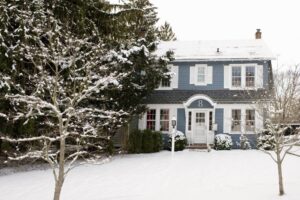 A blue and white two-story house with the number 8 above the door is surrounded by snow-covered trees and a snowy yard, capturing the peaceful spirit of Winter on a crisp day.