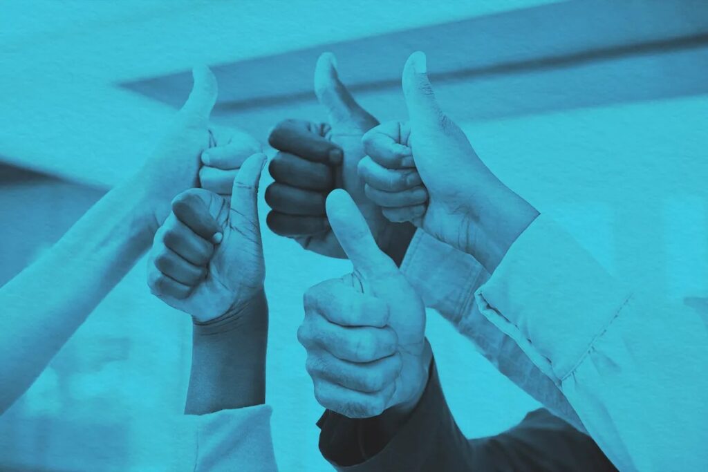 Several hands from different people giving a thumbs up gesture, symbolizing approval or agreement. The image has a blue tint, capturing the spirit of June Joys and new beginnings.