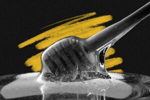 A close-up of a honey dipper covered in honey, with honey dripping into a glass container. The market for golden sweetness is heating up, set against a black background with a yellow brushstroke design behind the dipper.