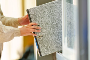 A person in a beige sweater places or removes a large gray binder from a shelf, both hands holding the spine—perhaps organizing documents for a December real estate update during the busy winter real estate season.
