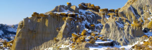 Snow-covered rock formations with layered, eroded cliffs and scattered large boulders under a clear blue sky evoke local folklore and tales whispered among the community.