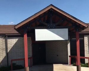 A brick building with a triangular roof supported by red posts and a blank white rectangular sign above the entrance, ready for June Joys and exciting celebrations.