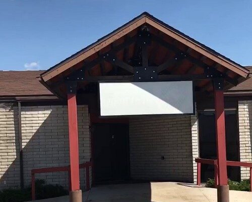 A brick building with a triangular roof supported by red posts and a blank white rectangular sign above the entrance, ready for June Joys and exciting celebrations.