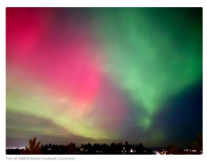 Bright green and pink aurora lights illuminate the winter night sky above a dark treeline, creating a vibrant and colorful natural display.