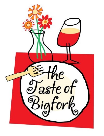 A white plate with the words the Taste of Bigfork, a fork, a wine glass, and a vase with three flowers are arranged on a red placemat, capturing the fresh spirit of the Spring season.