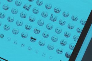 A digital screen displays various emoji faces, including happy, sad, confused, and cool expressions in rows against a blue-tinted background. A devices black edge is visible on the right side, adding a subtle winter glow to this Real Estate Update.