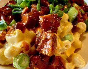 Close-up of macaroni and cheese topped with barbecue-sauced meat and sliced green onions—a vibrant, savory dish perfect for the Season of Action or savoring thoughtful August Reflections. The creamy cheese sauce ties all the flavors together beautifully.