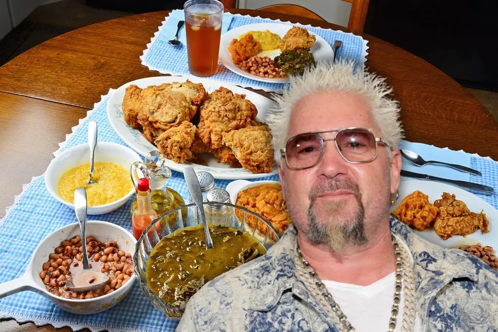 A man with blond spiked hair and sunglasses is smiling in front of a table set with Southern-style comfort food, savoring fried chicken, greens, beans, and cornbread during this August Reflections season.