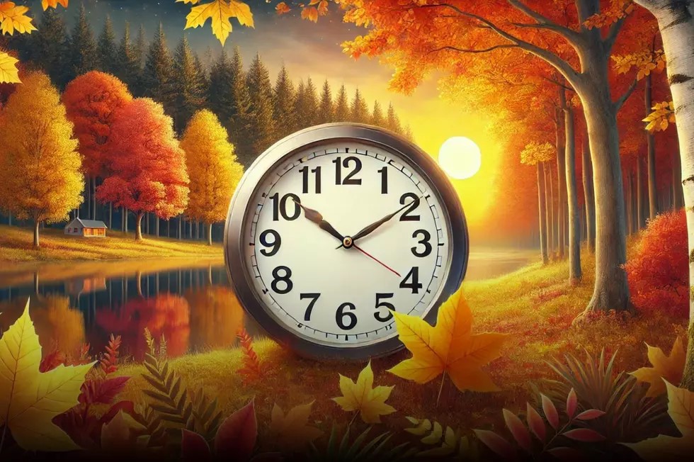 A large clock is set among colorful autumn leaves, with a forest of trees in red, yellow, and orange by a lake at sunset. The sun glows on the horizon during this crisp fall evening, and a small cabin appears in the background.