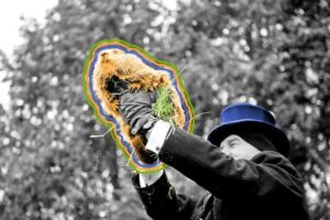 A person in a black suit and blue top hat holds up a groundhog, highlighted with colorful outlines, against a background of blurred trees—there’s love in the air as the scene brims with anticipation.