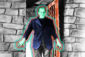 A person dressed as Frankenstein’s monster stands in a doorway with stone walls. The figure, inspired by classic folklore, has green skin and is outlined with colorful neon lines.